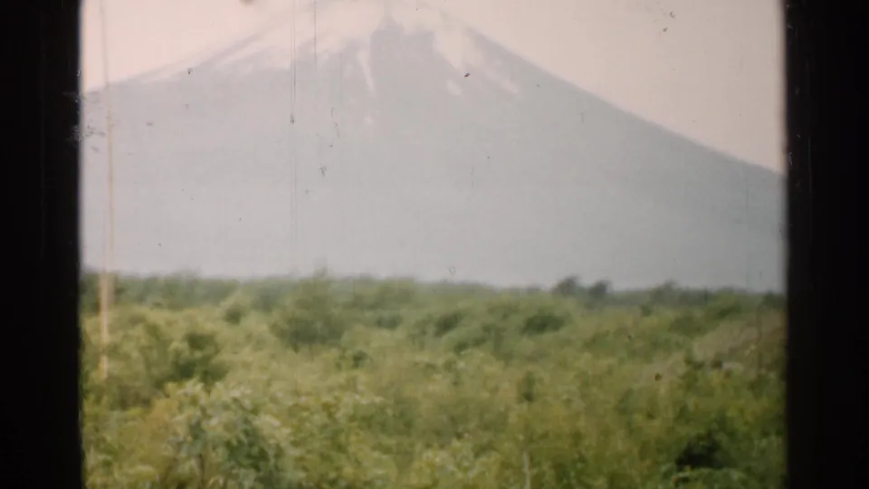 1952 Japan 8mm frame with the mountain slope softened by haze above a green field and low trees.