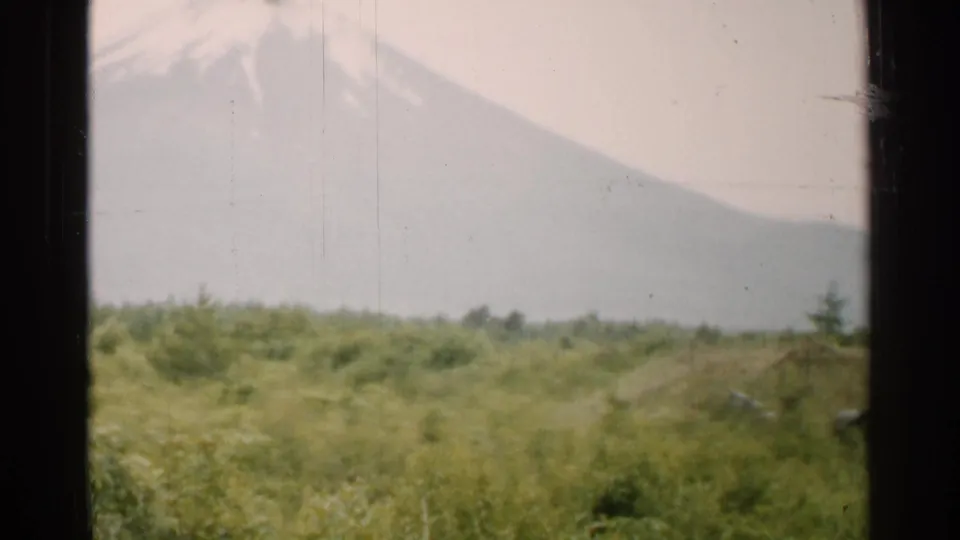 1952 Japan home-movie view of a mountain slope above fields, with low vegetation and a lighter strip at the right edge.