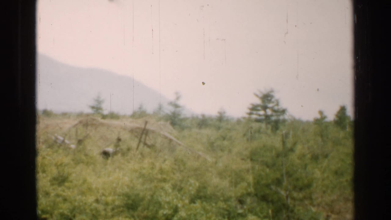 Grassy field with distant hills seen through a dark 8mm frame border.