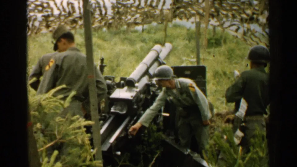 Soldiers in olive drab uniforms and steel helmets work around a field cannon in a camouflaged Japanese field position.