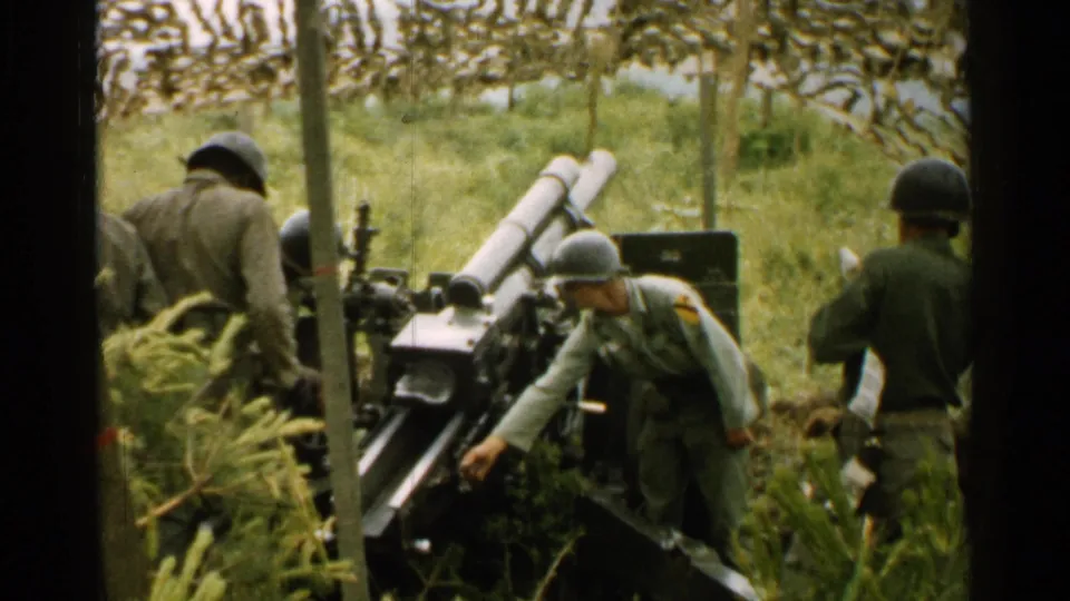 A group of soldiers in helmets and field uniforms handle or prepare artillery equipment in a grassy position in Japan.