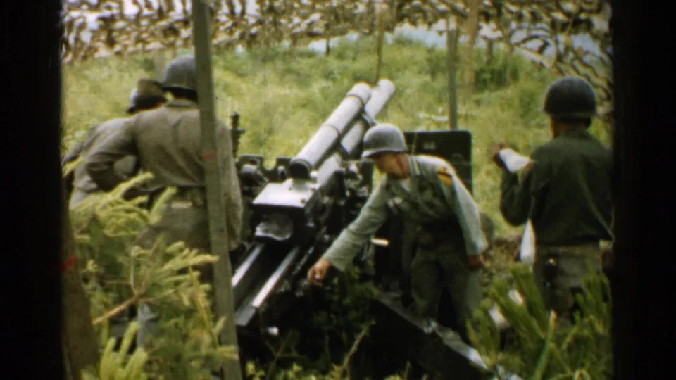 1952 Japan footage frame with several uniformed soldiers beside a field cannon, one holding papers or cloth near the right edge.