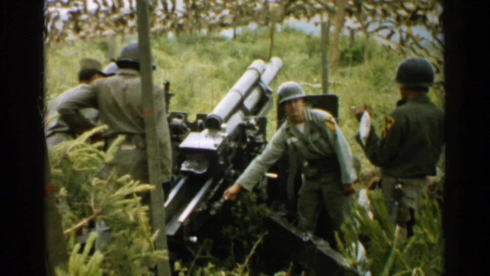 1952 Japan 8mm frame showing a soldier reaching to adjust or touch a field artillery piece as other helmeted soldiers watch nearby.