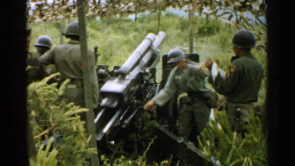 U.S. soldiers in 1952 Japan appear to adjust or load an artillery cannon surrounded by trees and tall grass.