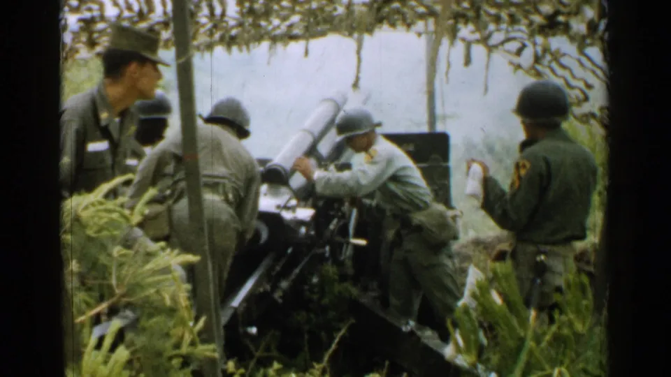 In this 1952 Japan frame, soldiers operate a field gun with pale smoke or blast haze visible behind the artillery piece.