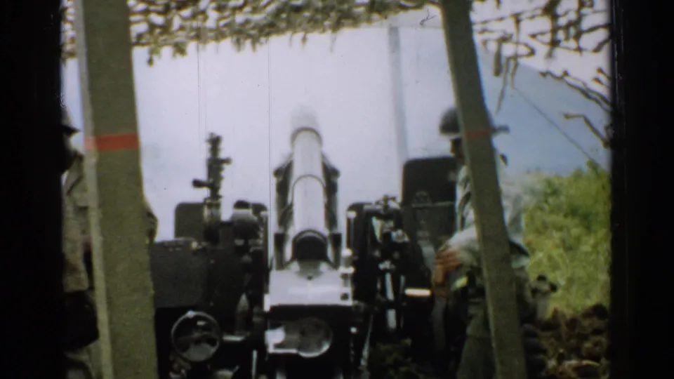 The cannon is seen from the front after firing, with smoke in the background and soldiers partly visible at the edges.