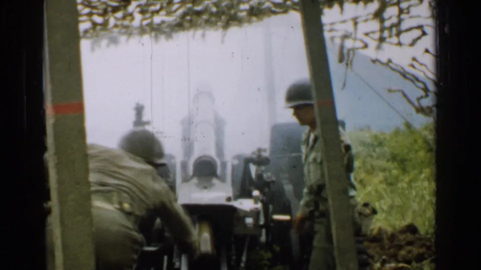 1952 Japan 8mm frame showing helmeted soldiers around an artillery cannon in a brushy field position.
