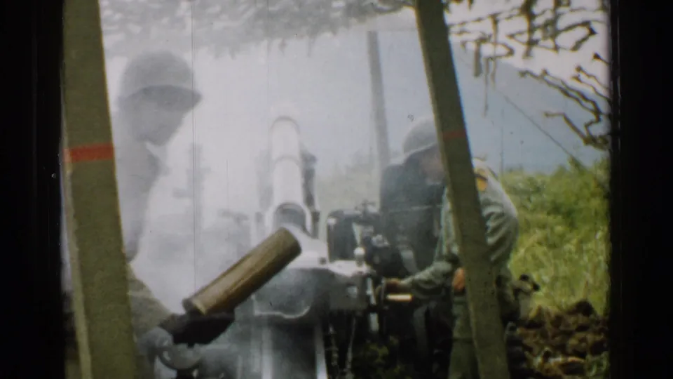 1952 Japan 8mm frame showing a helmeted soldier handling a shell beside an artillery cannon in smoke.