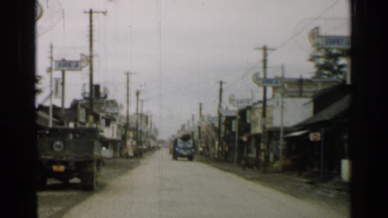 Town street with a military truck ahead, utility poles, shopfronts, and signage.