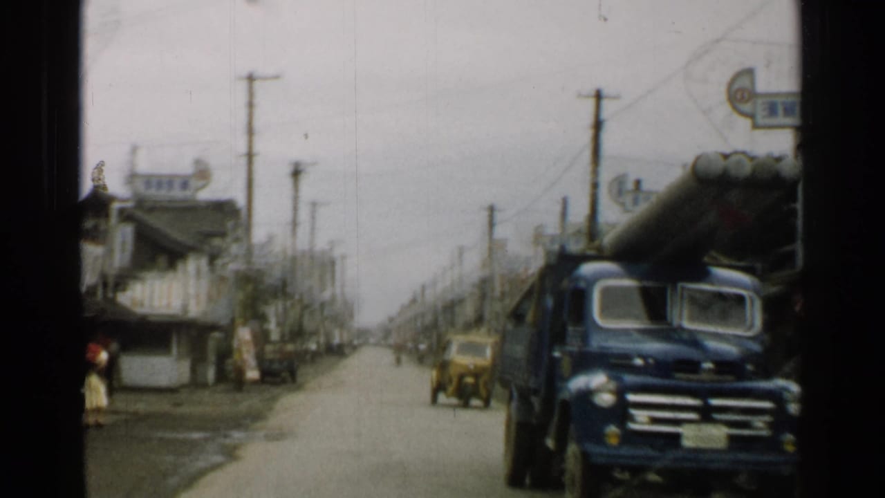 Blue truck passes near the camera as a yellow vehicle appears farther down the road.