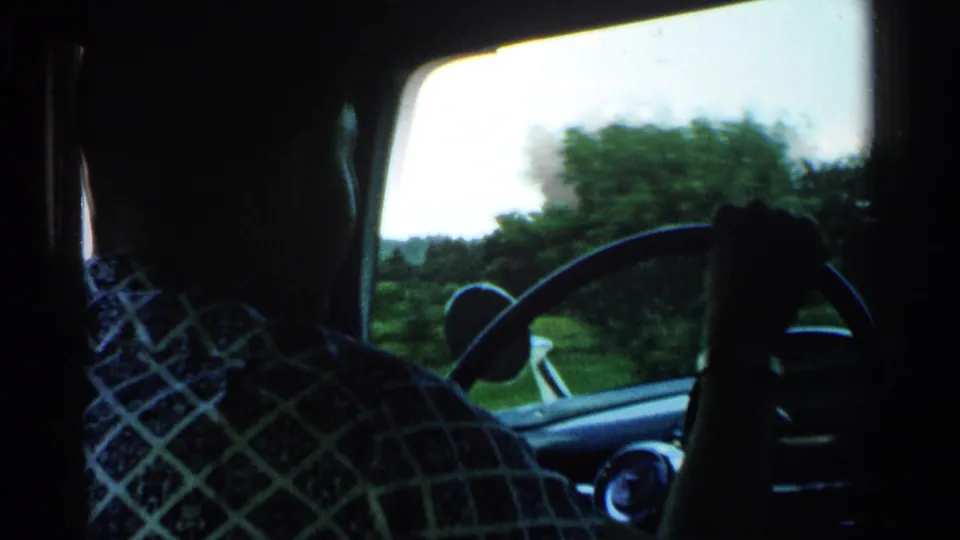 Rear-seat view of a silhouetted driver at the wheel, with roadside trees and fields outside in 1952 rural Japan footage.