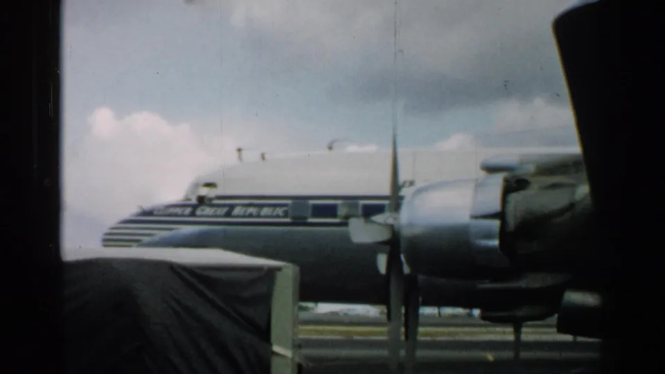 A parked propeller aircraft on a Japan tarmac, with visible aircraft markings and cloudy sky in 1952 home-movie footage.