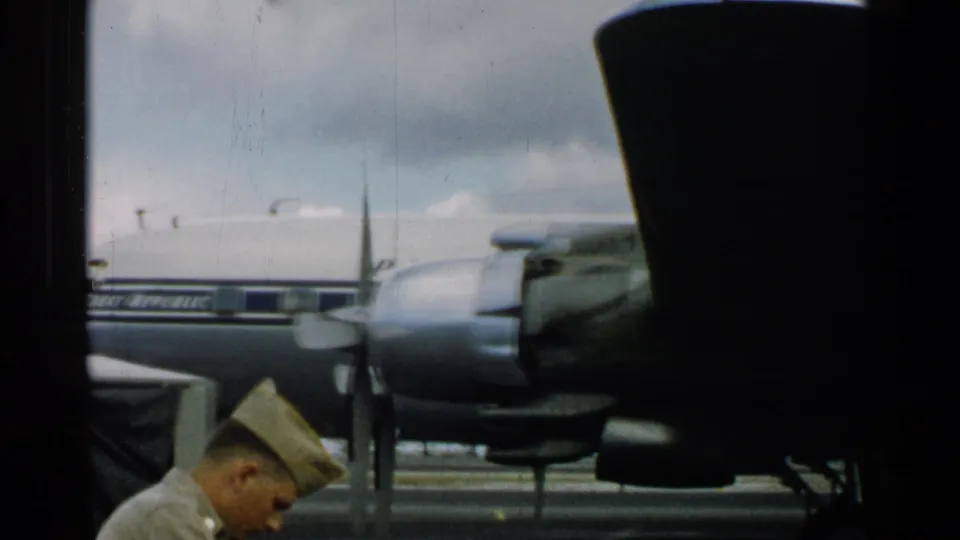 A uniformed airman crosses the foreground below a parked propeller aircraft on a Japan airport tarmac in 1952 footage.