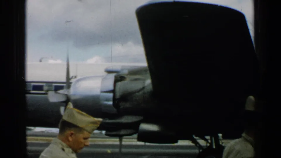 In Japan in 1952, uniformed men stand beside a propeller aircraft engine and dark aircraft structure under a cloudy sky.