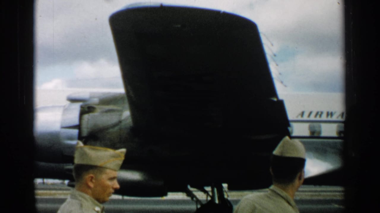 Men in light uniforms stand by aircraft with partial fuselage lettering behind them.