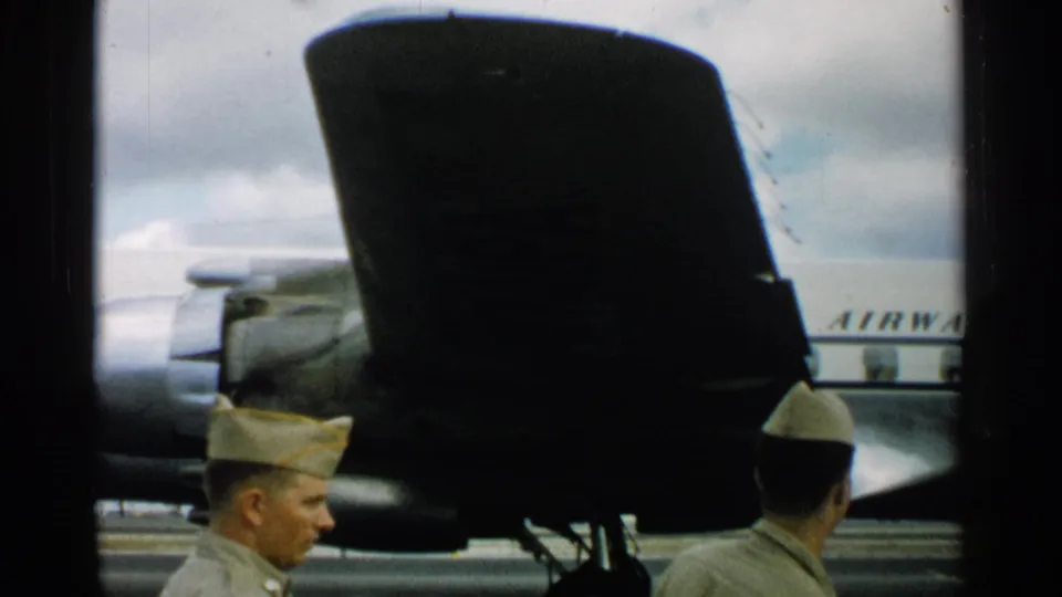 Uniformed men at a 1952 Japan airfield stand beside a dark aircraft section, with partial AIRWA lettering visible on a white fuselage behind them.