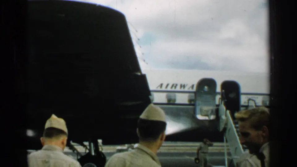 Several uniformed men at a 1952 Japan airfield stand near aircraft, with partial fuselage lettering and open aircraft doors visible in the background.