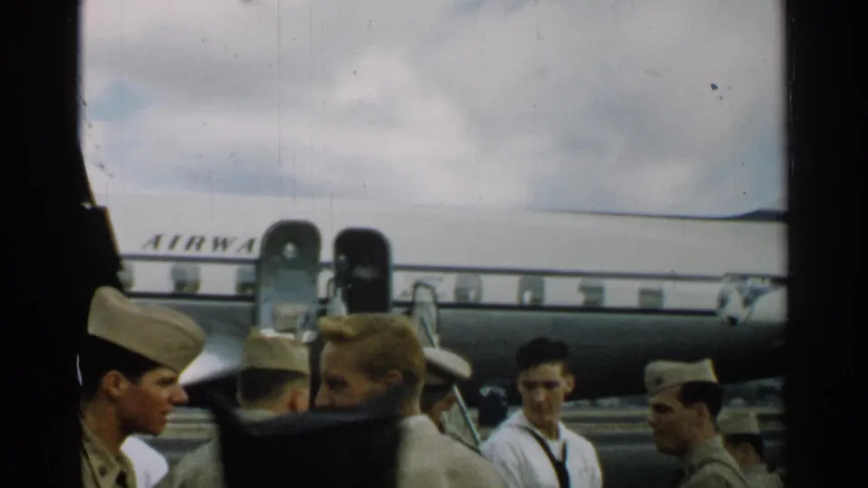 A home-movie view shows uniformed personnel, including a sailor-like figure, near a Pan Am aircraft during boarding in Japan, 1952.