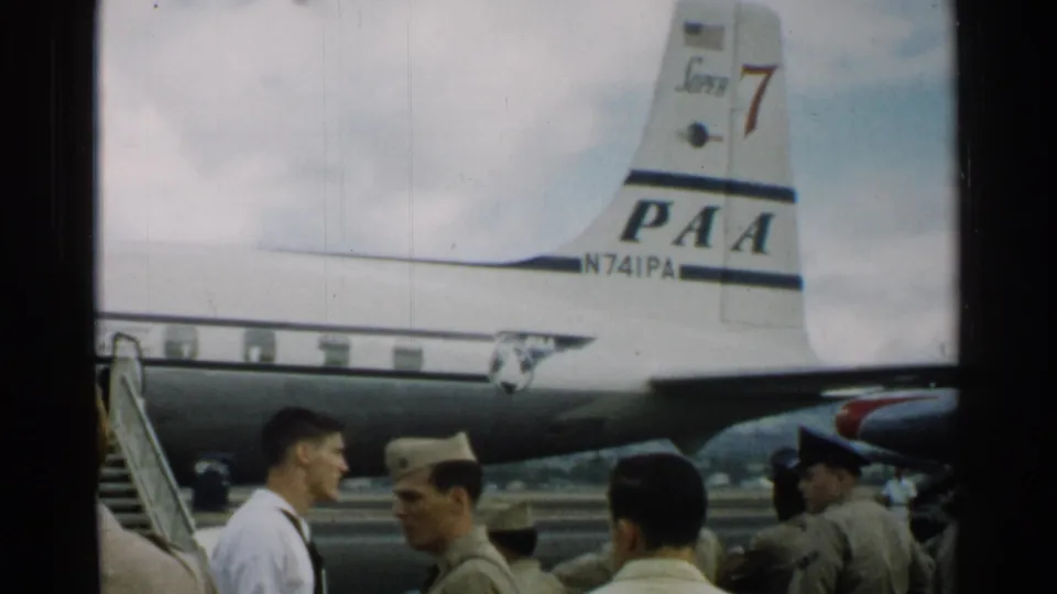 Uniformed men on a Japan airport tarmac stand below the tail of a Pan American aircraft in this 1952 frame.