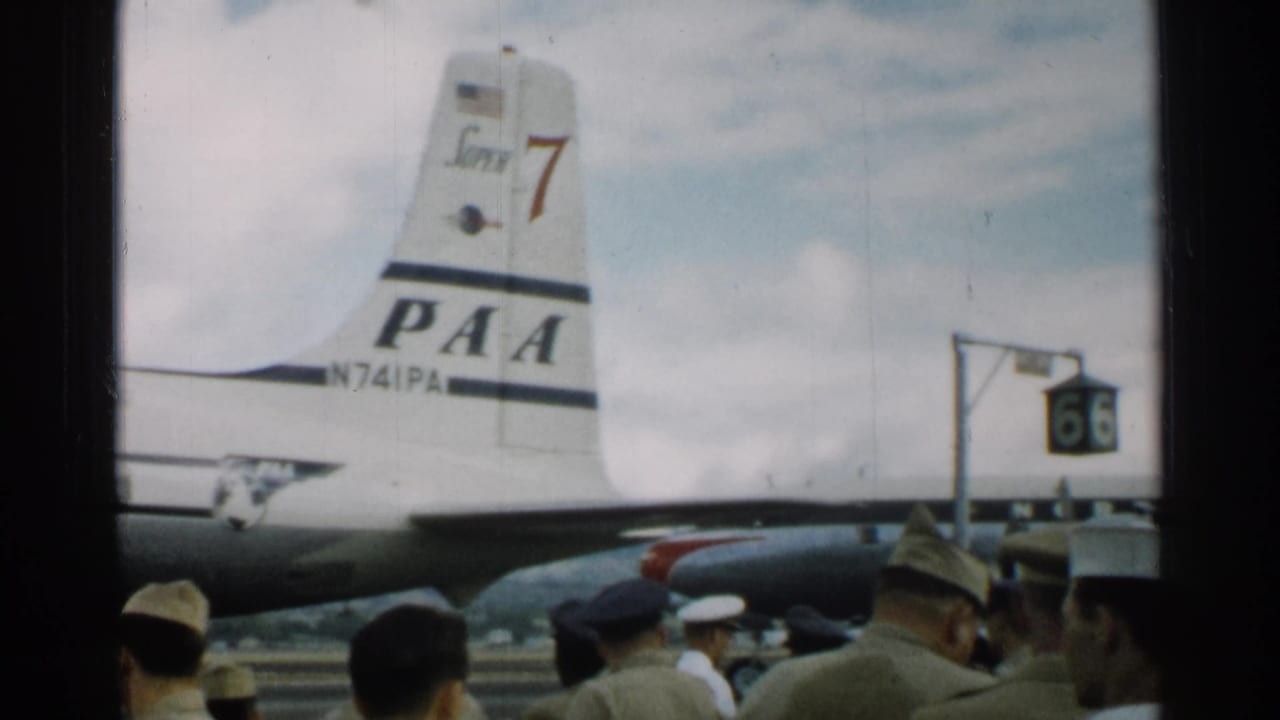 1952 Japan 8mm frame showing a PAA aircraft tail marked N741PA behind uniformed personnel and civilians at an airfield.