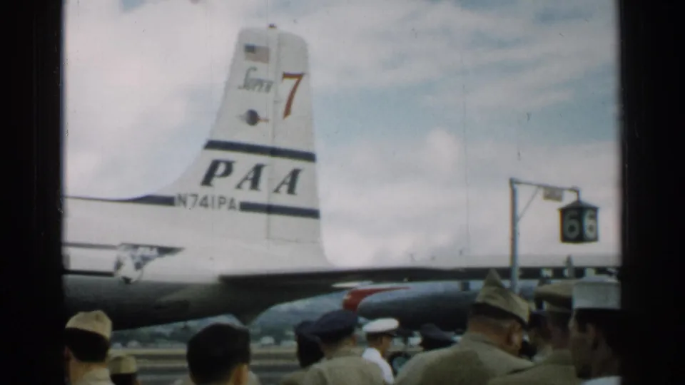 1952 Japan 8mm frame showing a PAA aircraft tail marked N741PA behind uniformed personnel and civilians at an airfield.