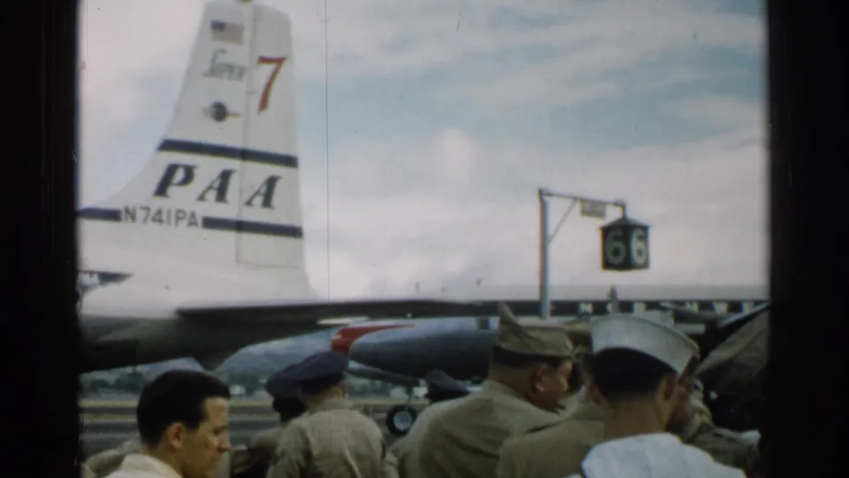 1952 Japan airfield view with PAA tail markings, uniformed men, civilian faces, and a sign marked 66 near the aircraft.