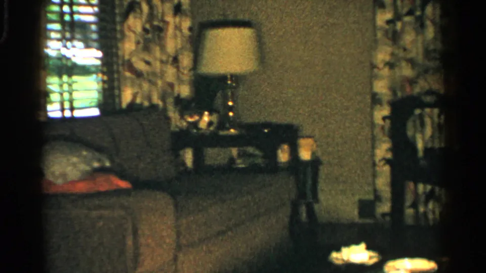 1952 Japan home interior with couch, pillows, side table lamp, patterned curtains, blinds, and small items near the foreground.