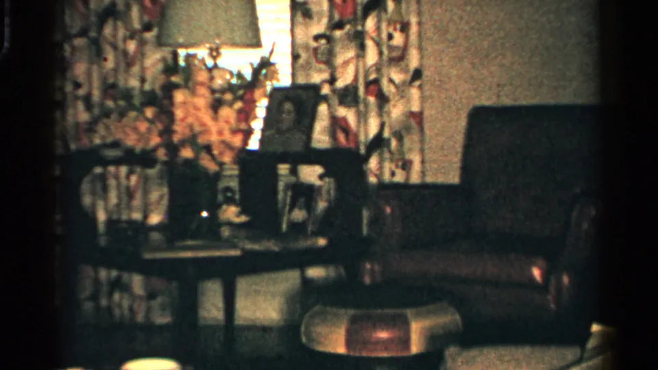 1952 Japan domestic interior with a lamp, patterned curtains, framed portraits, flowers, and seating arranged around a table.