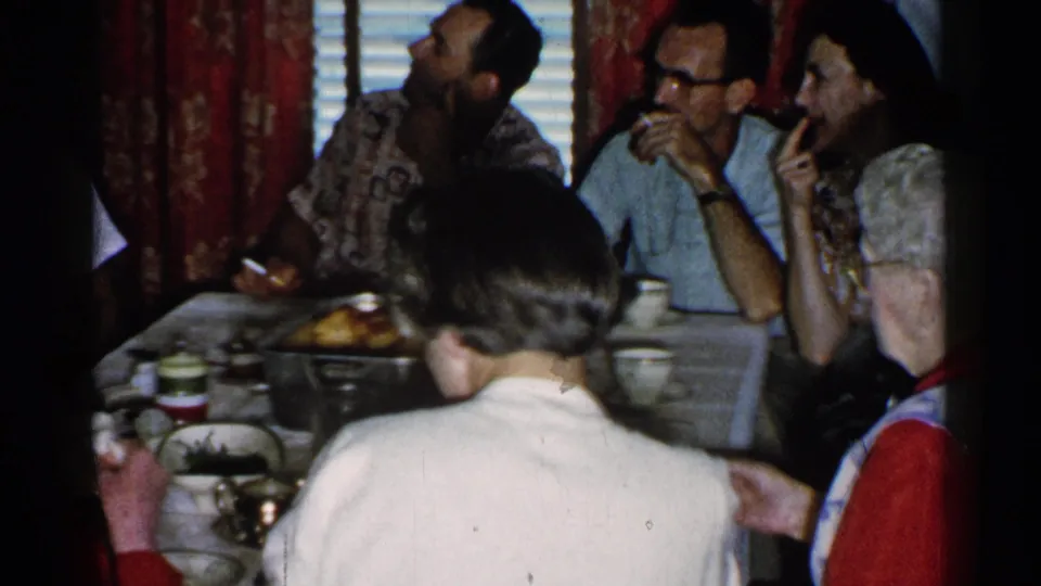 Adults at a private dinner table in Japan appear to talk and smoke, with tableware, red curtains, window blinds, and wallpaper in view.