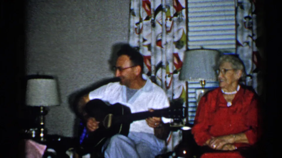 New Hampshire 1952 living-room frame with a man holding a guitar and an older woman seated beside him.
