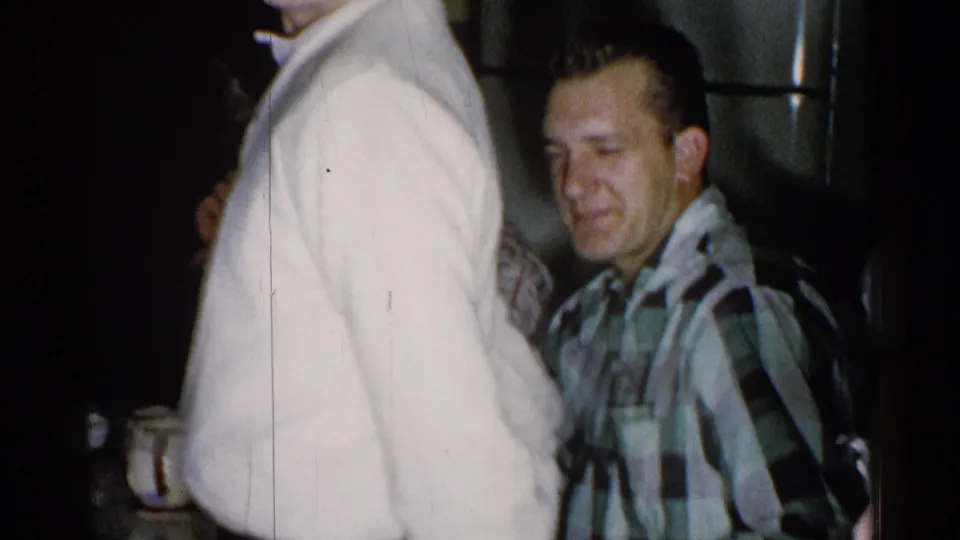 1952 New Hampshire home interior showing a seated man in a plaid shirt partly obscured by someone in a white sweater.