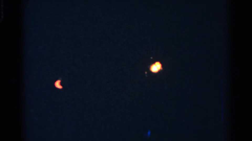 Dark, grainy 8mm frame with soft red and warm holiday lights, likely near the Christmas tree in the 1952 New Hampshire clip.