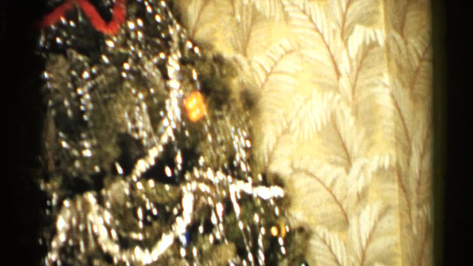 1952 New Hampshire home-movie frame showing a decorated Christmas tree with silver tinsel, ornaments, warm lights, and patterned wallpaper.