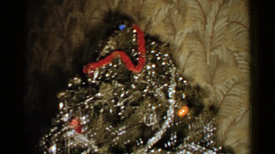 Close 8mm view of the decorated Christmas tree with silver tinsel, red ribbon, ornaments, and patterned wallpaper in the 1952 New Hampshire footage.