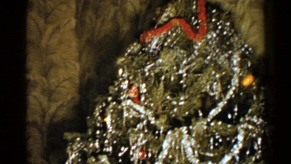 1952 New Hampshire home-movie frame showing a close, soft-focus view of a Christmas tree with heavy silver tinsel, ornaments, and red ribbon.