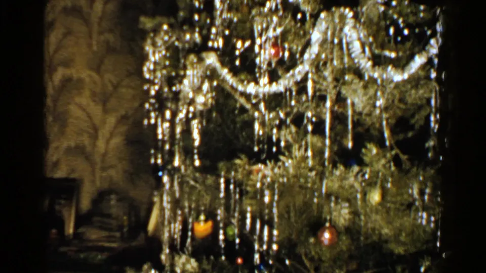1952 New Hampshire home-movie frame showing dangling silver holiday decorations and ornaments on a Christmas tree inside a private room.