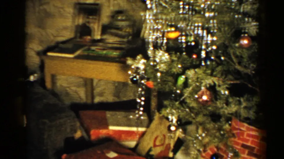 1952 New Hampshire home-movie frame showing a decorated Christmas tree, a small table with objects, and wrapped presents arranged underneath.