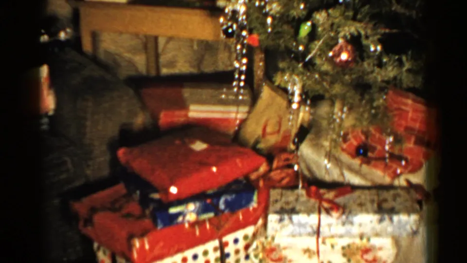 1952 New Hampshire home-movie frame showing wrapped Christmas presents beneath a tinsel-covered tree in a private home interior.