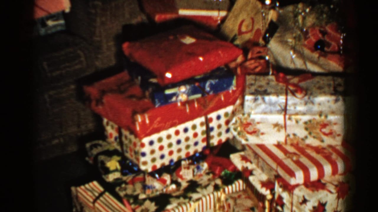 1952 New Hampshire 8mm frame showing wrapped Christmas presents stacked near holiday decorations in a dim home interior.