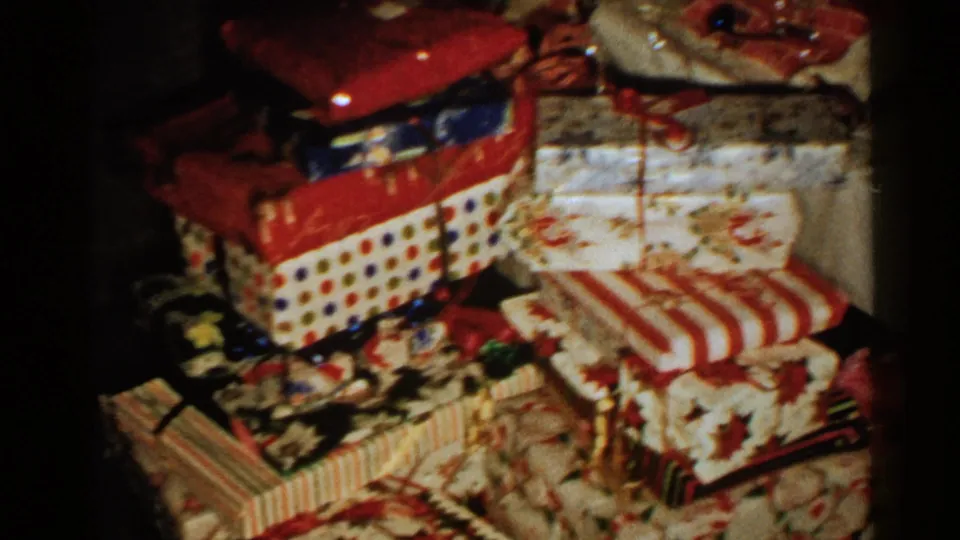 1952 New Hampshire home-movie frame of a Christmas present pile with red bows and varied wrapping paper.