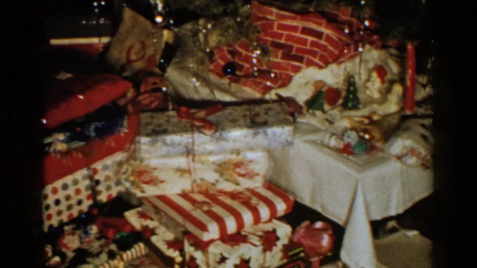 1952 New Hampshire 8mm frame showing wrapped gifts, a white side table, ornaments, and a brick-patterned holiday backdrop.