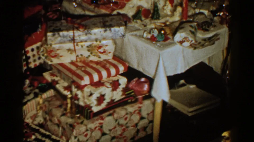 1952 New Hampshire home-movie frame of Christmas presents arranged beside a white table with small ornaments and tinsel.