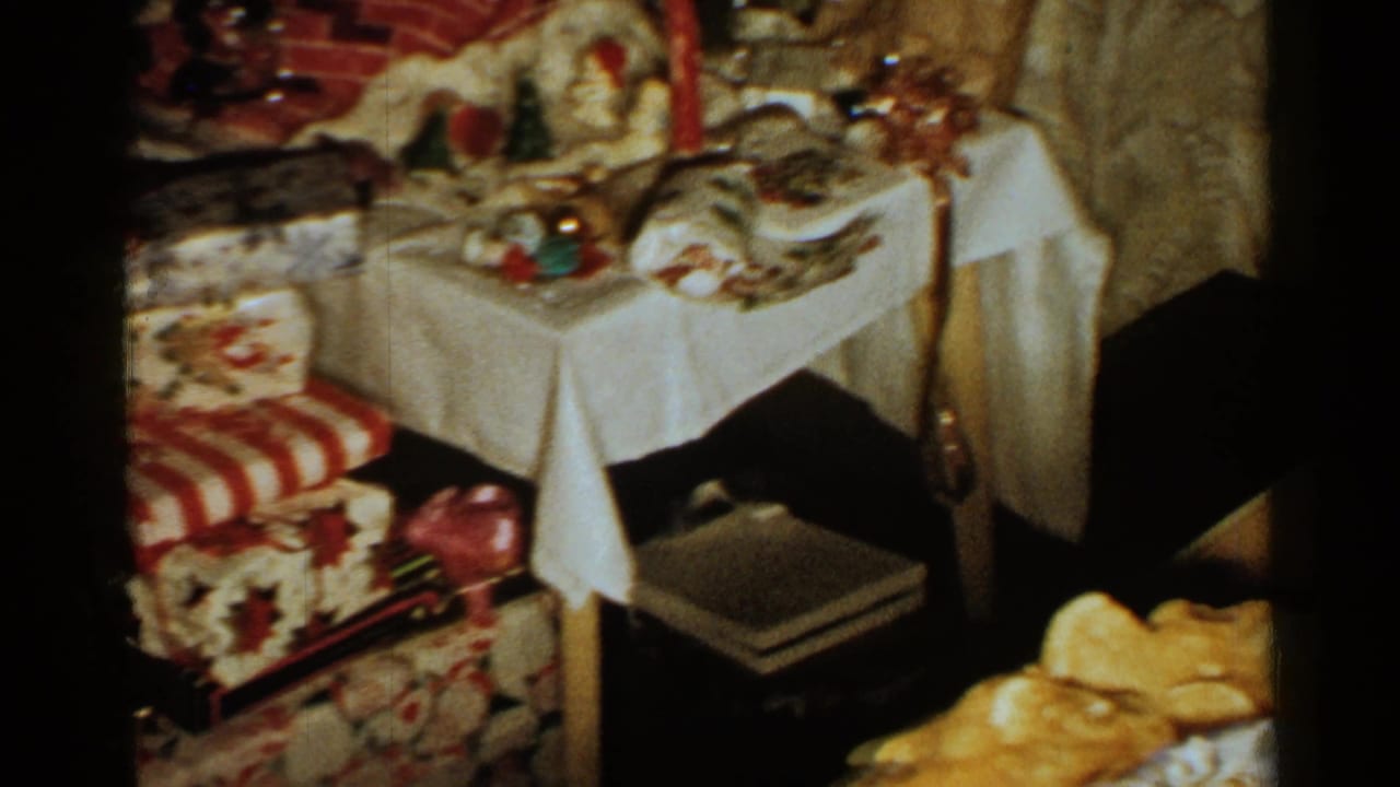 1952 New Hampshire home-movie frame showing wrapped Christmas presents, a small table with a white cloth, and patterned seating in a private interior.