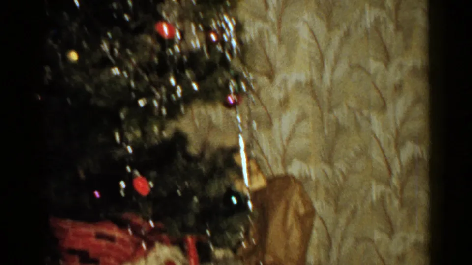 1952 New Hampshire home-movie frame of a Christmas tree with silver tinsel and colored ornaments in a warmly lit private room.