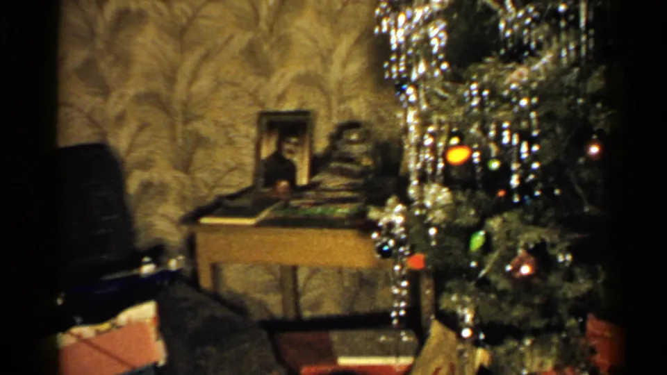 1952 New Hampshire home-movie frame showing a decorated Christmas tree, gifts, a chair, a small table, and a framed portrait in a private interior.