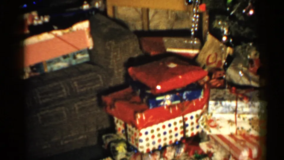 1952 New Hampshire home-movie frame focused on holiday presents stacked by a couch with the Christmas tree partly visible at the edge.