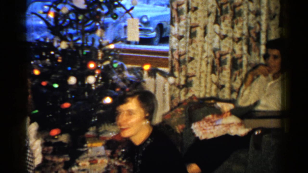 Women seated in a living room near a lit Christmas tree and wrapped presents.