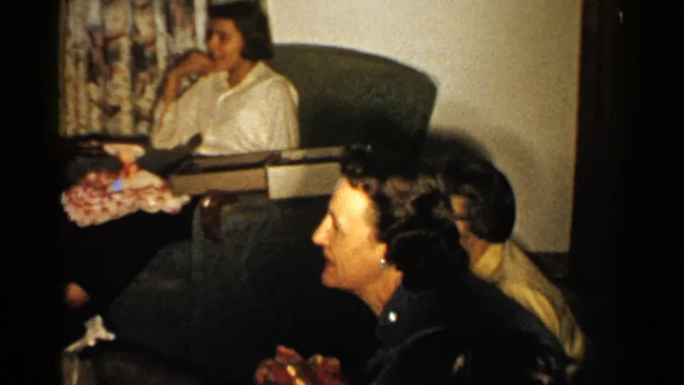 A 1952 New Hampshire Christmas gathering frame with several women seated indoors, wrapped presents nearby, and patterned curtains behind them.
