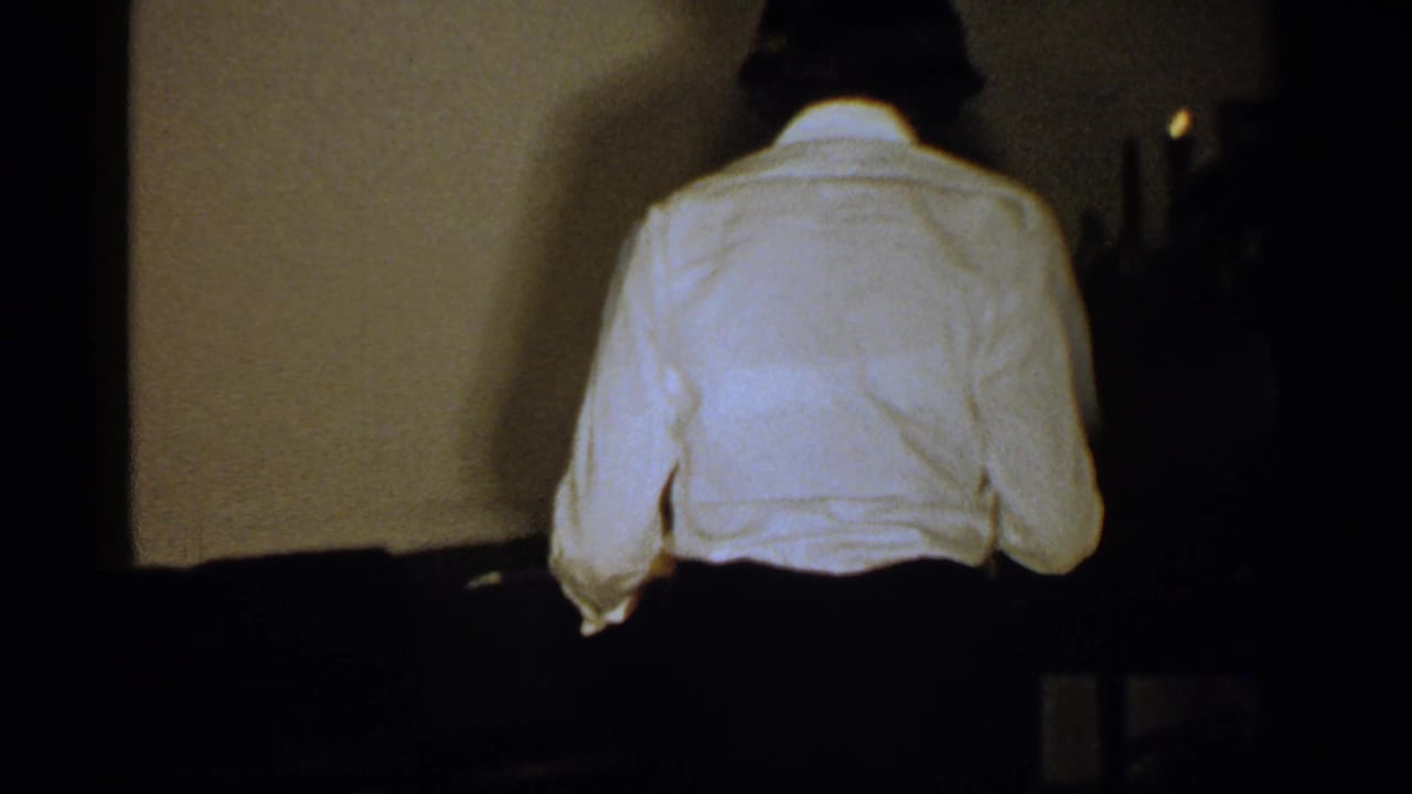 Person in a white shirt seen from behind in a dark living room.