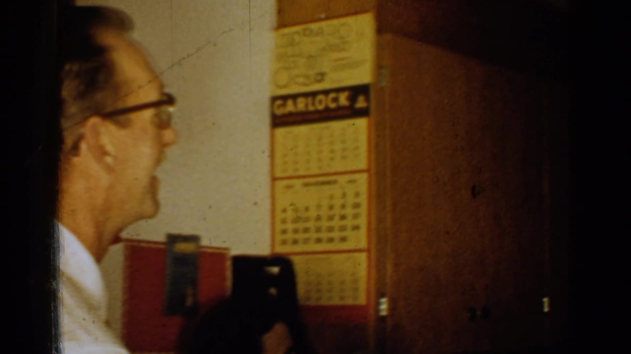 Older man indoors seen in profile near a Garlock calendar and wooden doorway.